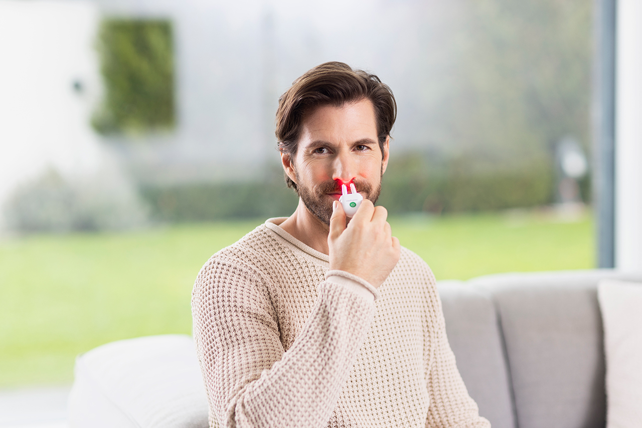 Man using the medisana medinose compact by inserting the light therapy device into his nose.